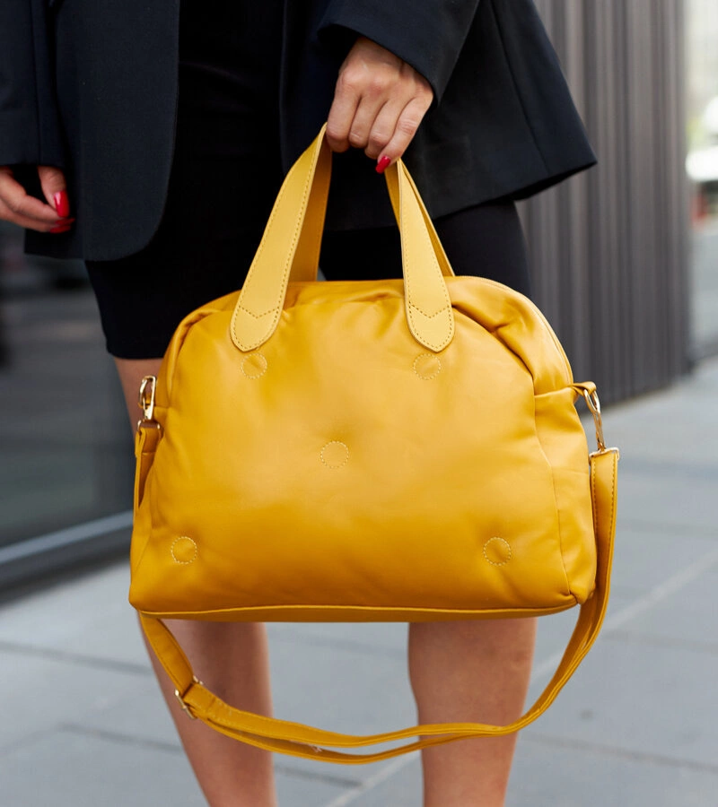 Žlutá pikovaná kabelka na rameni Ruaydy.